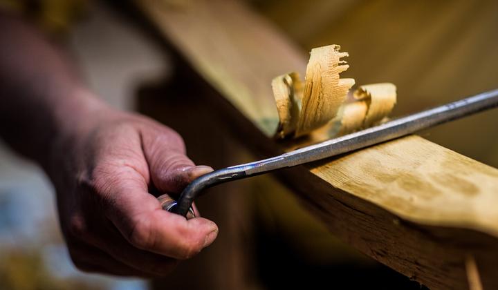 Eine Hand zieht mit dem Zugmesser Späne von einem Bogenholz